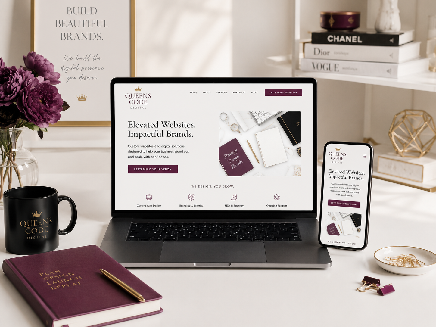 Queens Code Digital workspace with laptop, phone, plum accents, flowers, black mug, and white desk